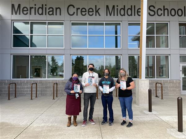 Four staff members take a picture outside Meridian Creek Middle School holding calculators. 